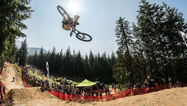 Mountain biker mid-air performing tricks for a crowd of onlookers.