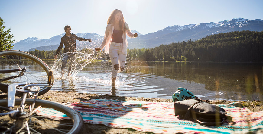 A couple splashing in the water at the edge of a lake in Whistler