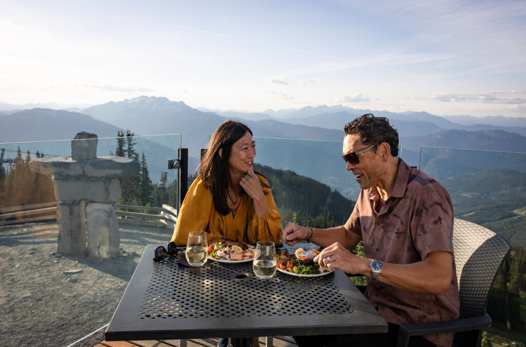 The Inuksuk behind a couple enjoying lunch at the Roundhouse Lodge on Whistler Mountain.
