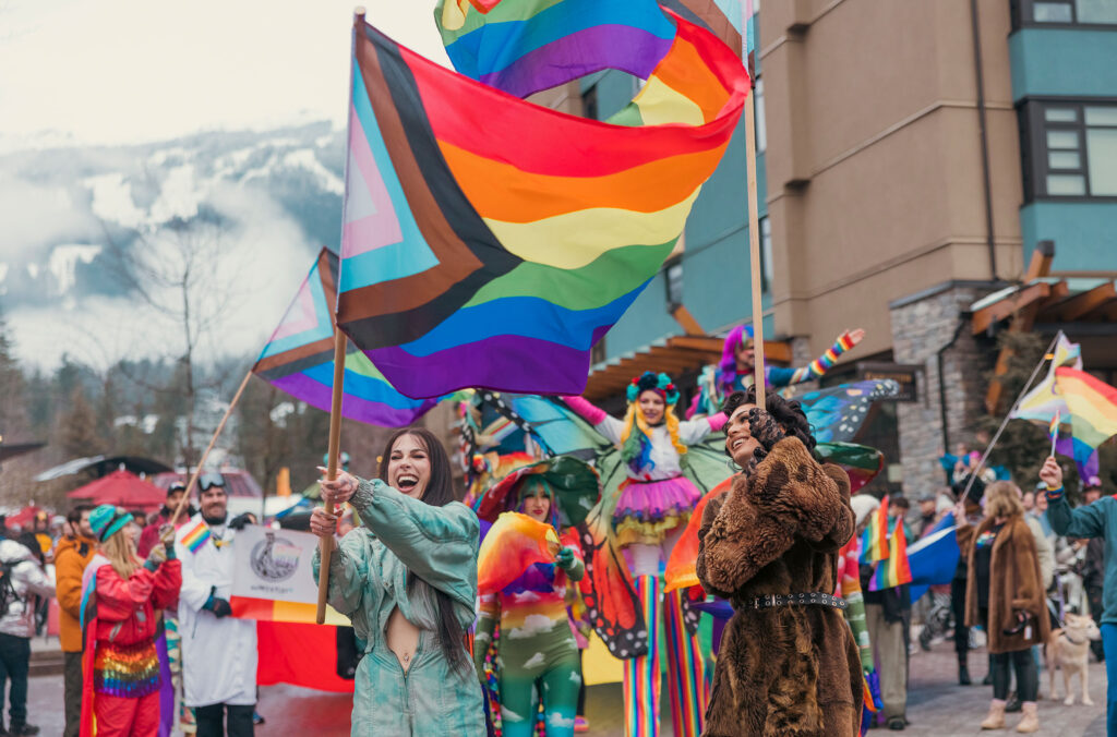 A colourful parade with rainbow flags flying as people celebrate the Whistler Ski and Pride Festival.