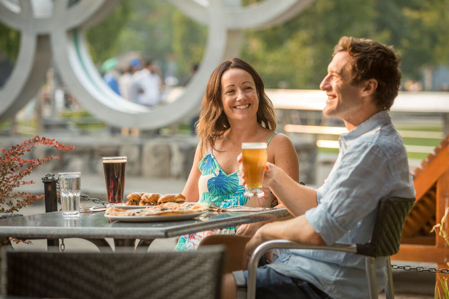 A couple enjoys a drink and a bite to eat in front of the Olympic Rings in Whistler Village. 