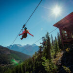 A zipliner soaring above the trees on a sunny day in Whistler.
