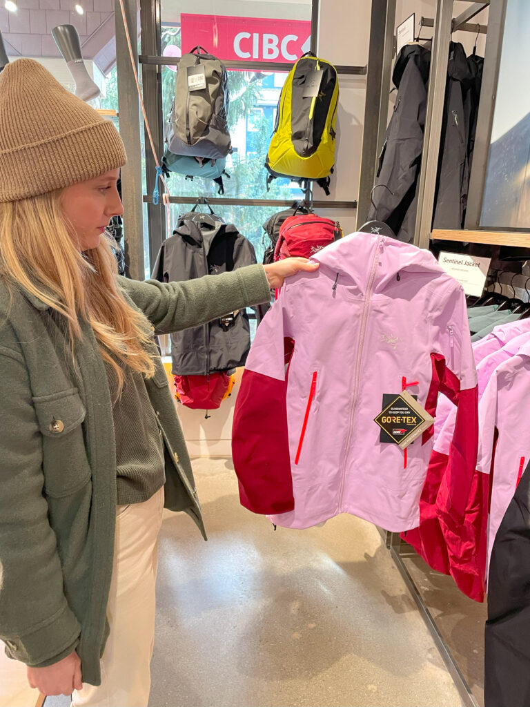 Brittany holds up a pink and red Arc'teryx jacket in the Whistler store.