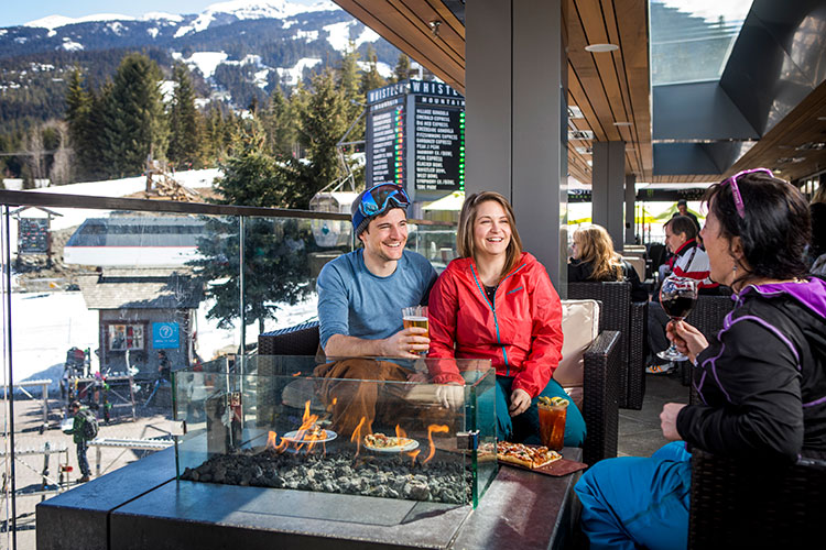 A couple enjoy apres in Whistler on a sunny bar patio.