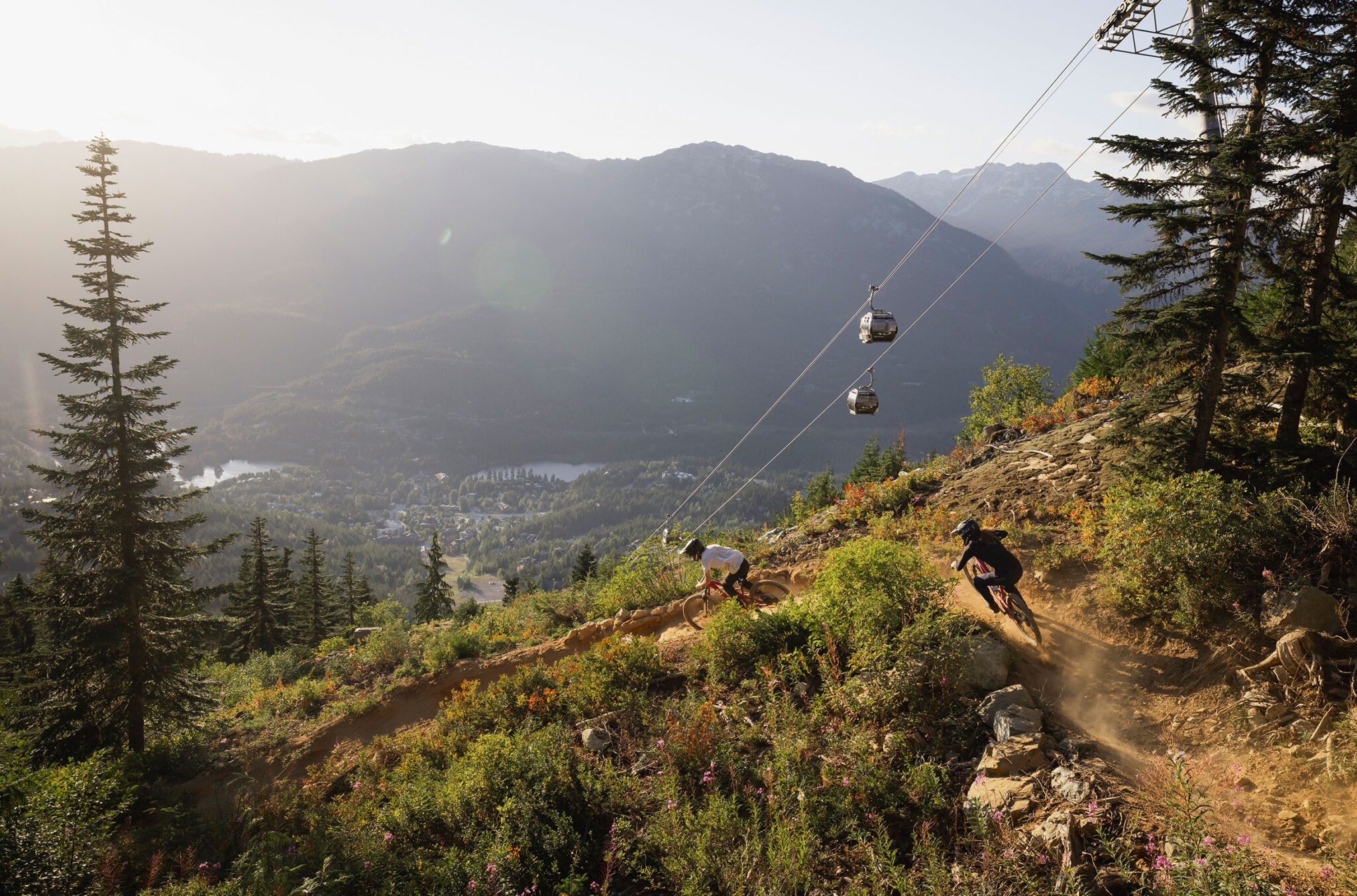 A shot of two downhill mountain bikers riding the trails under the Creekside Gondola in the Creekside Zone of the Whistler Mountain Bike Park.