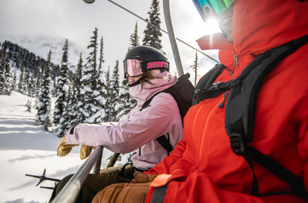 Two skiers sit on a chairlift in the sun on Whistler Blackcomb.