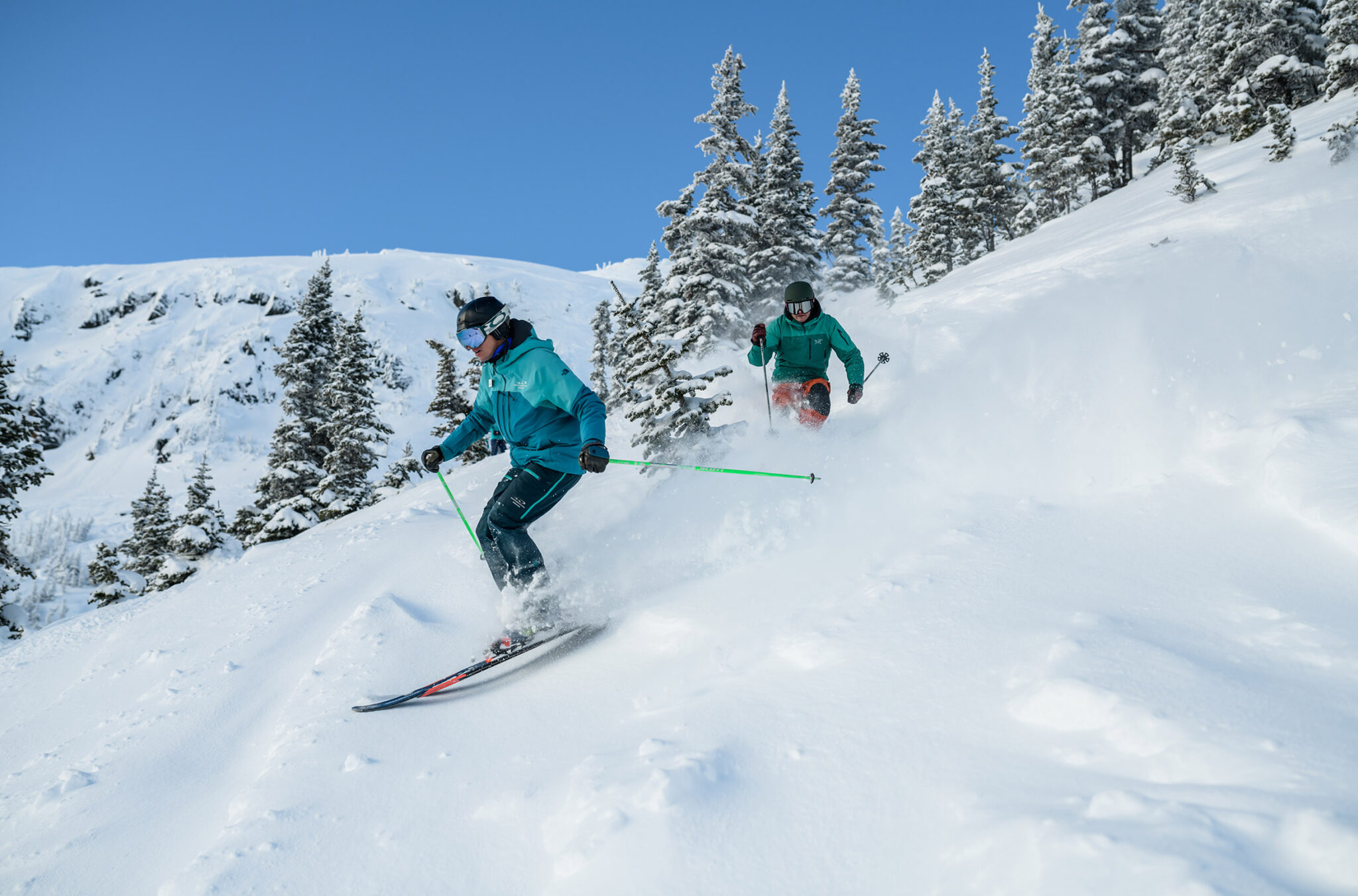 A ski instructor takes some turns in the powder with a student following behind.