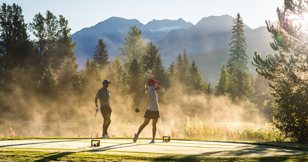 Two golfers play in the spring mist on a Whistler golf course.