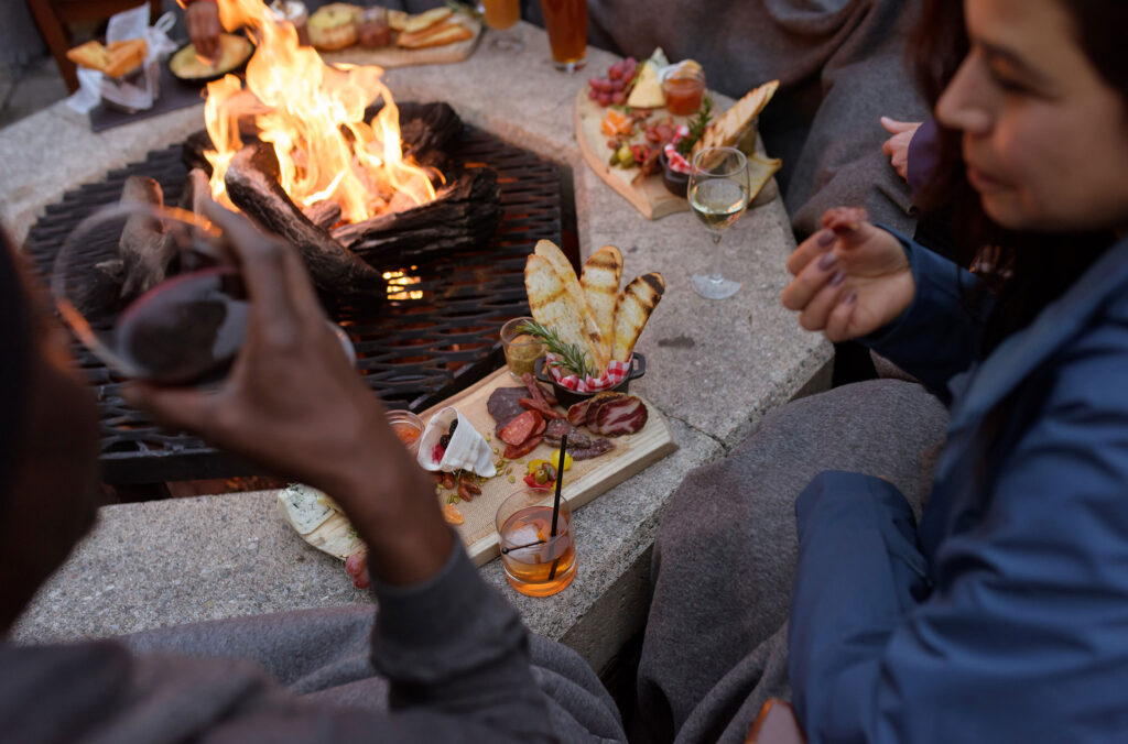 A group sits round an outside firepit with yummy food.