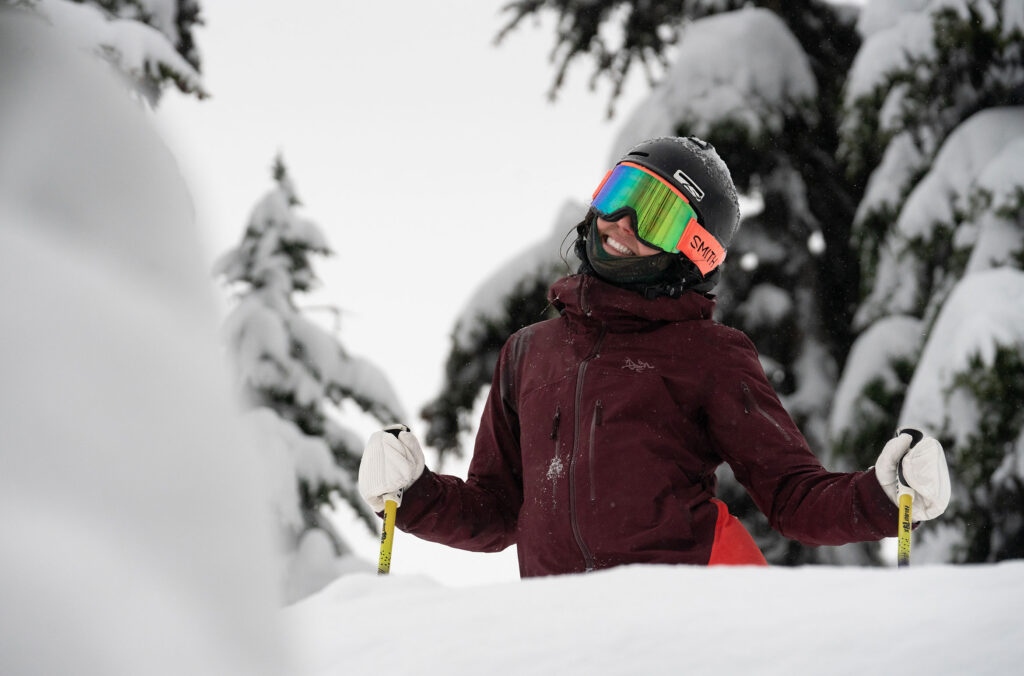 A skier smiles at the camera before hitting some powder on a tree run on Whistler Blackcomb.