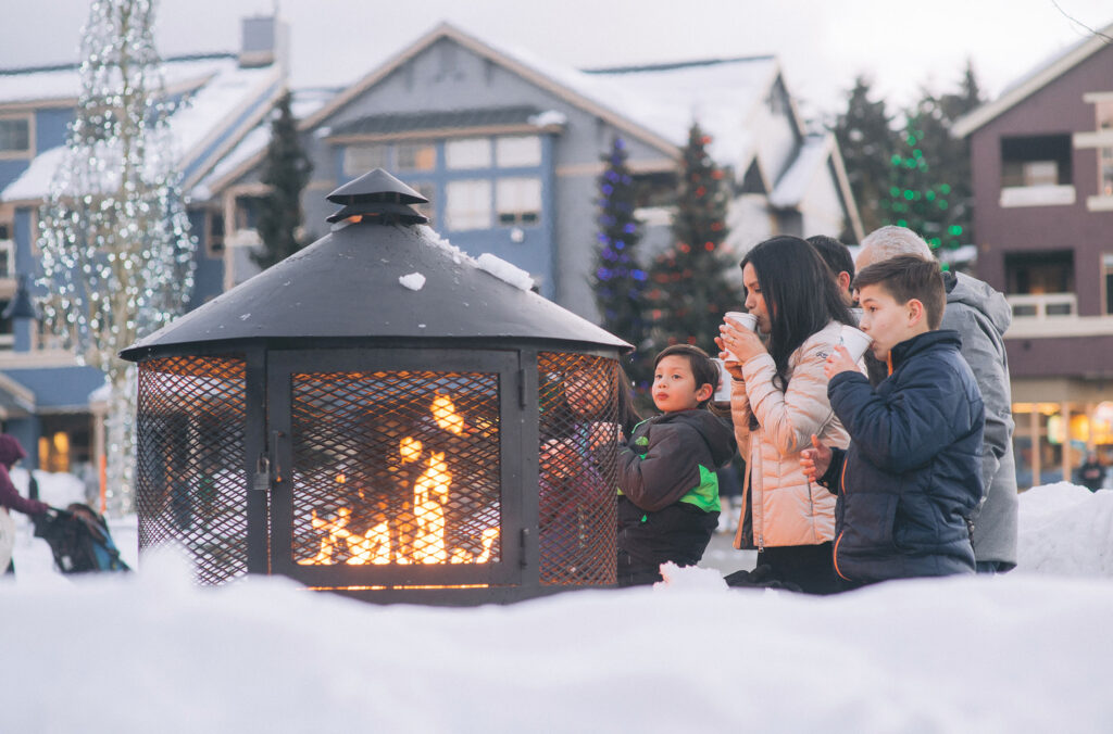 A family drink hot chocolate around the fire at Whistler Olympic Plaza.