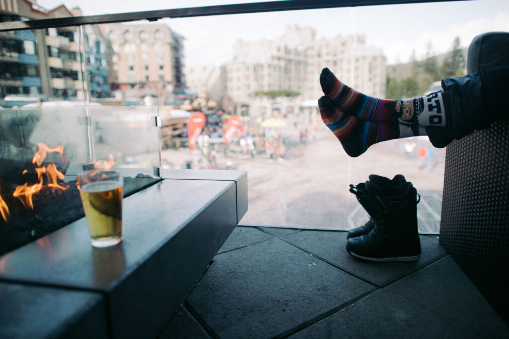 Someone warms their feet at an outside fire on the patio of the GLC in Whistler.