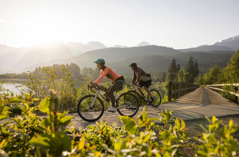 Two bike riders enjoy the Whistler Valley Trail around Green lake in the spring sun.