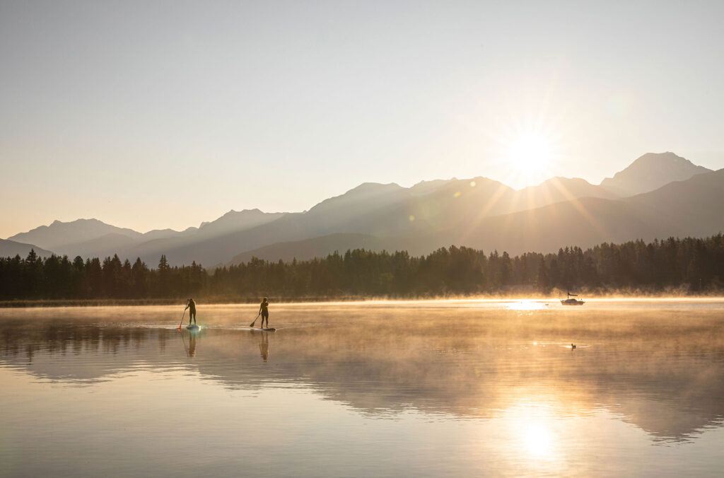 Two paddle boarders make their way across a lake in Whistler in the summer sun.