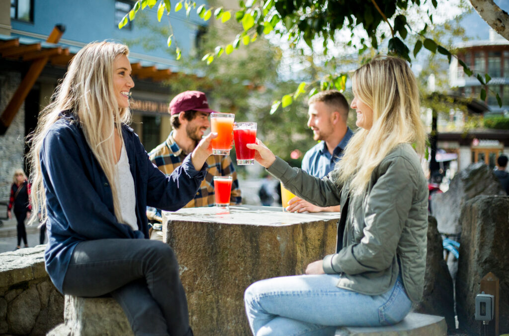 Friends sit on a sunny, fall patio in Whistler drinking craft beers.