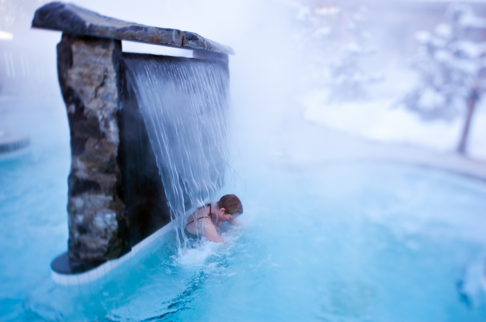 A man in a steamy pool under a waterfall.