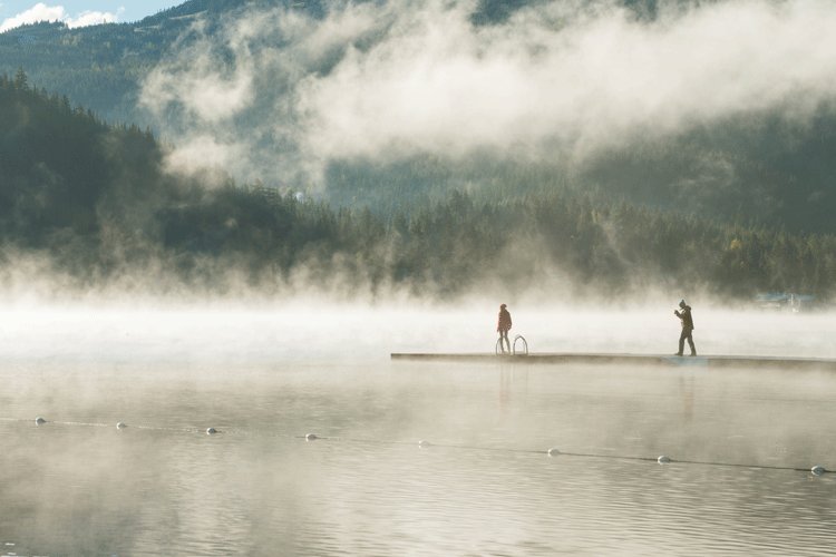 Two people standing on a dock on a misty lake.