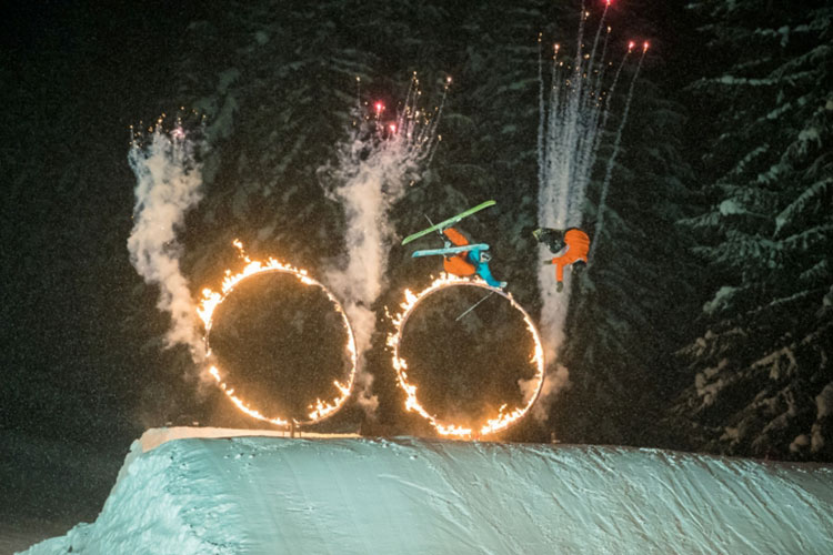 skiers and snowboarders jumping through flaming hoops