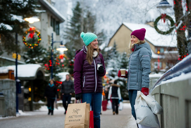 Two women chatting while walking with shopping bags down the village stroll.