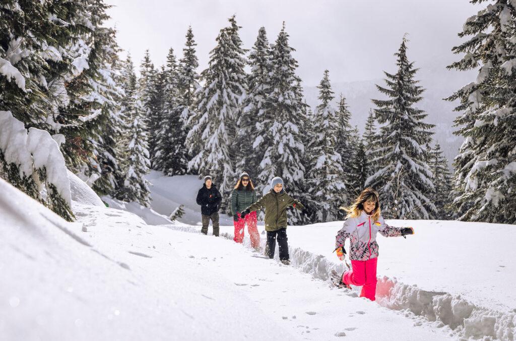 A family snowshoes in the Callaghan Valley at Whistler Olympic Park. The snow is deep and bright.