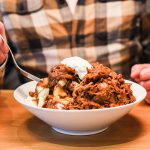 A big bowl of poutine topped with pulled pork and sour cream.