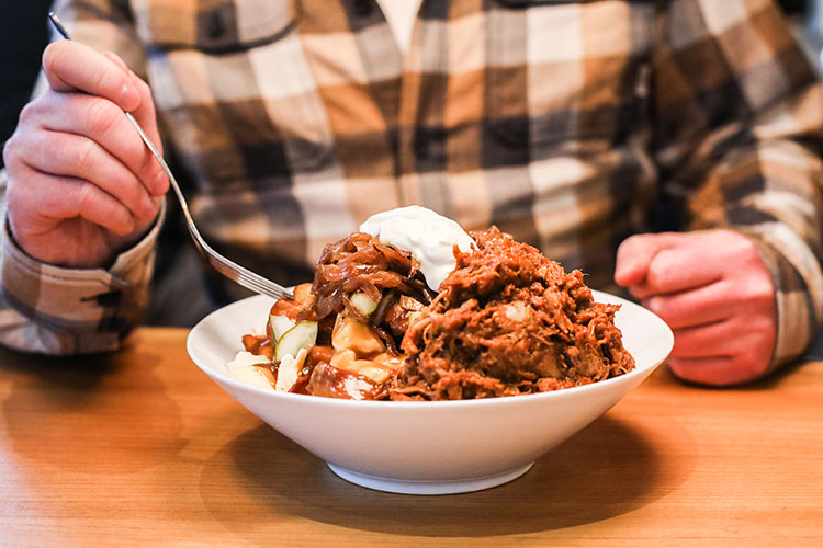 A big bowl of poutine topped with pulled pork and sour cream.