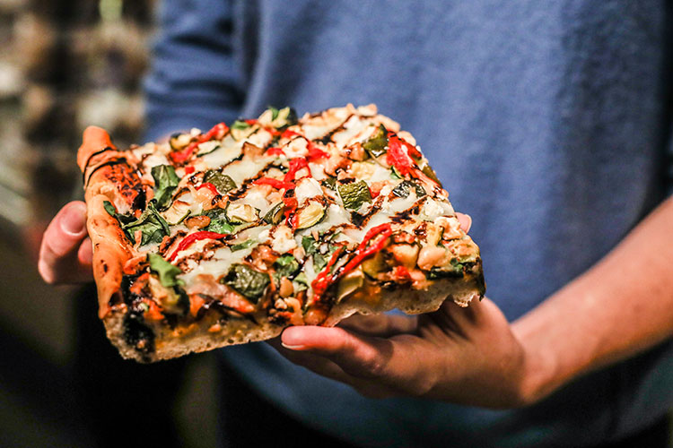 A large slice of pizza with goats cheese, tomatoes, and balsamic reduction.