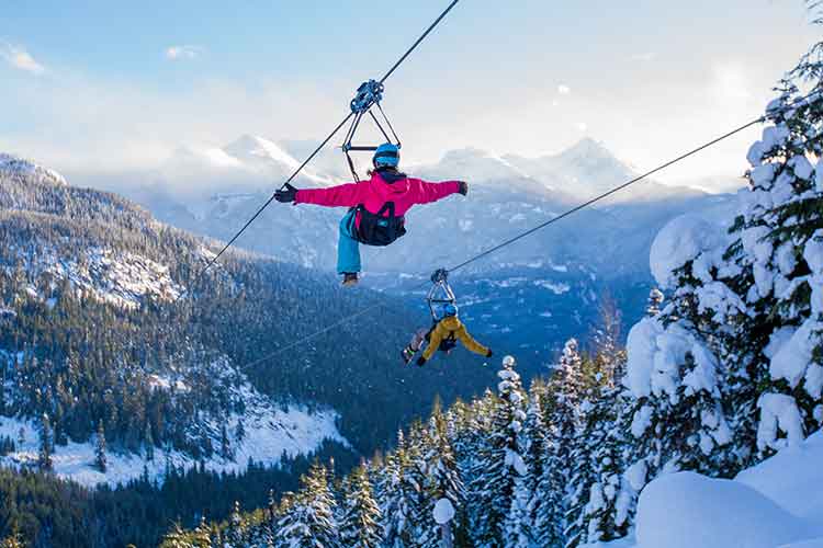 two people ziplining over snowy trees 