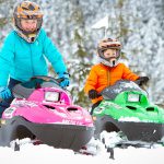 Two kids on mini z snowmobiles.