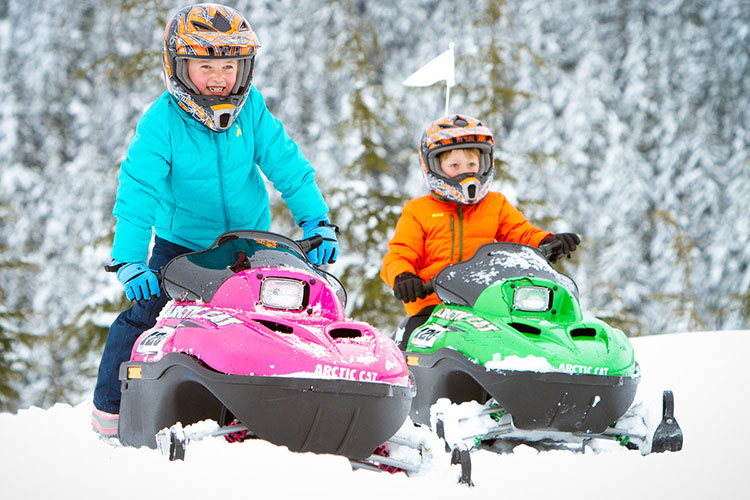 Two kids on mini z snowmobiles.