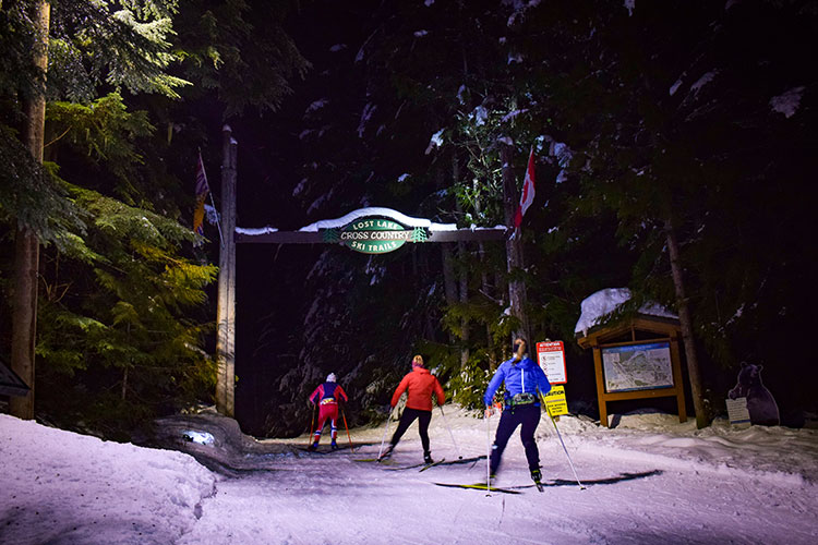 Three cross-country skiers head off on the Lost Lake trails at night in Whistler.