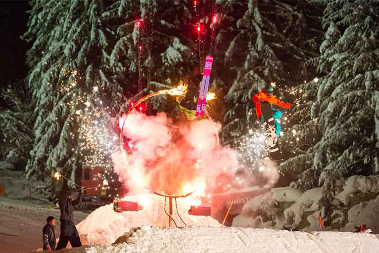 Skiers and boarders jump through a ring of fire.