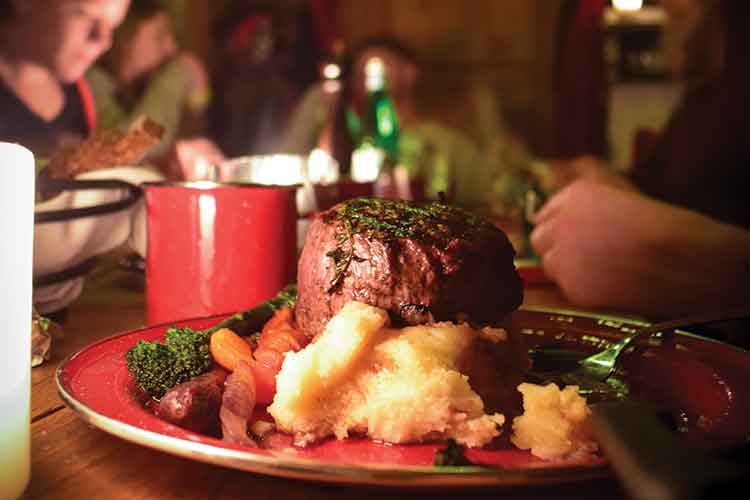 Steak dinner on a bed of mashed potatoes and vegetables.