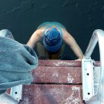 A swimmer enters the cold waters of a Whistler lake, edging down a metal stairs and breaking the ice.