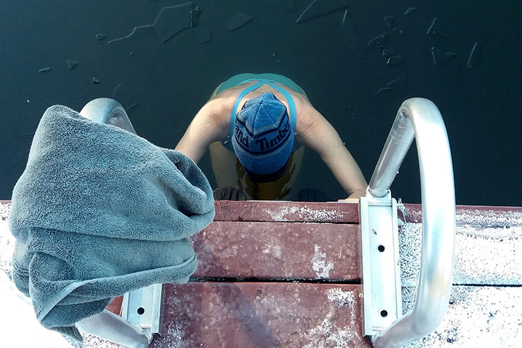 A swimmer enters the cold waters of a Whistler lake, edging down a metal stairs and breaking the ice.