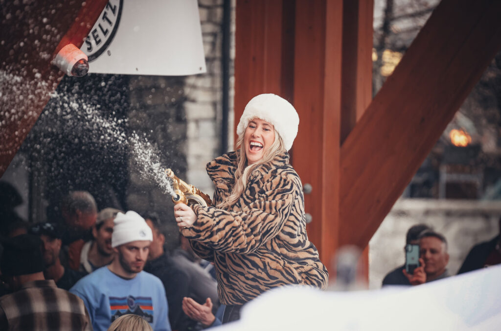 A women dressed in a fluffy animal print coat pops a Champagne bottle on the patio of the Longhorn Saloon in Whistler. Party time at WSSF.