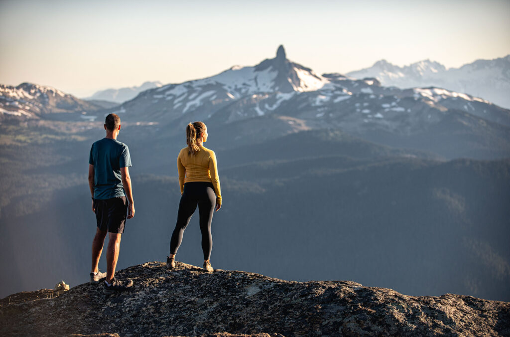 Two hikers look at the view from the top of Whistler Mountain out over to Black Task in the summer.