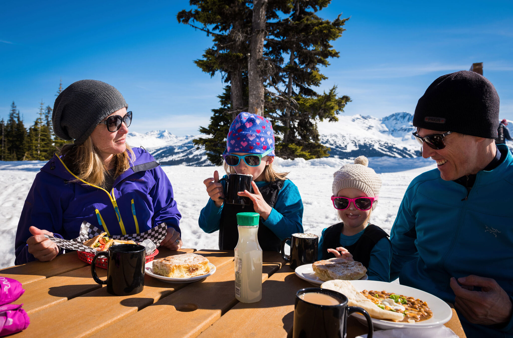 A family with two young children enjoy lunch up the mountains in Whistler on a sunny, winter day.