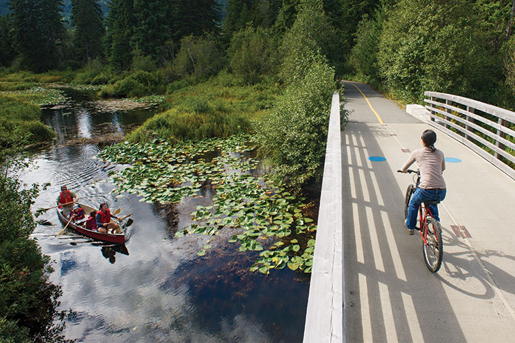 A family canoes down the River of Golden Dreams as a biker crosses the bridge above.