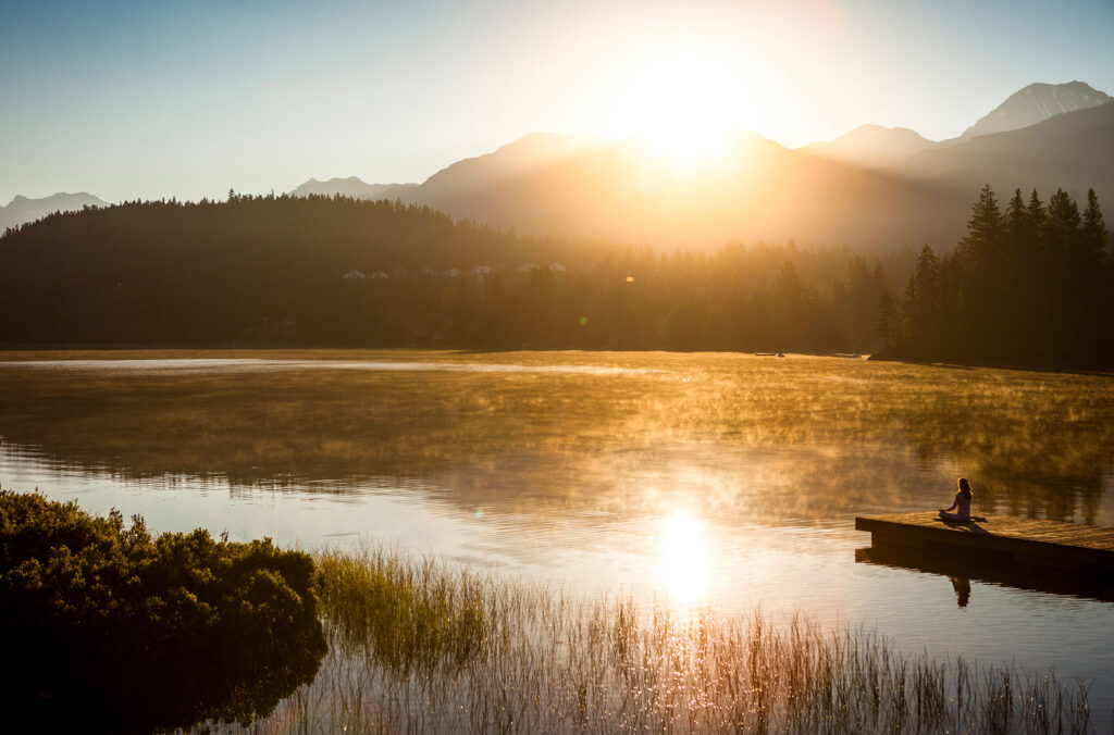 A woman meditates at the end of a dock over looking a lake in Whistler.