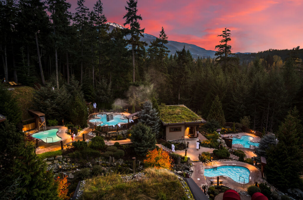 A shot of the Scandinave Spa in the pinky hues of the fall alpen glow. Outdoor hot pools sit amidst the old growth forest.