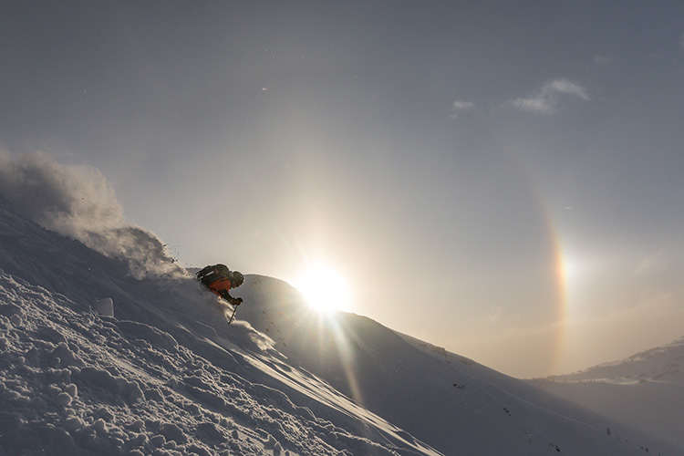 Skiier in front of a peak with a sun dog in the background