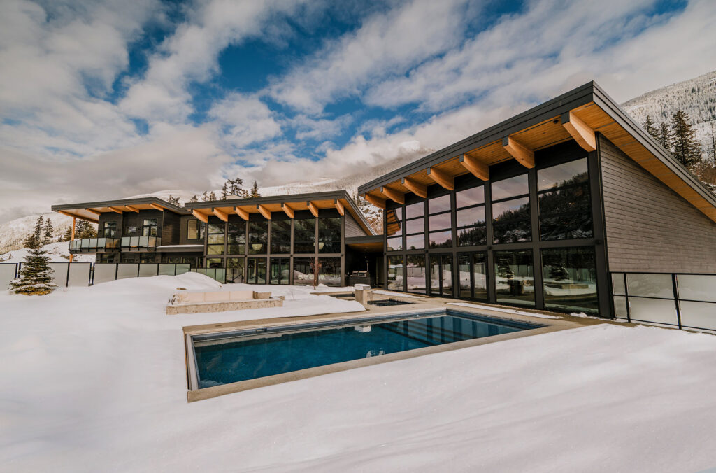 Wedge Mountain Lodge & Spa as seen from the outside with the ground covered in snow. The lodge is modern and chic, with a lot of glass windows and a pool extending out the back.