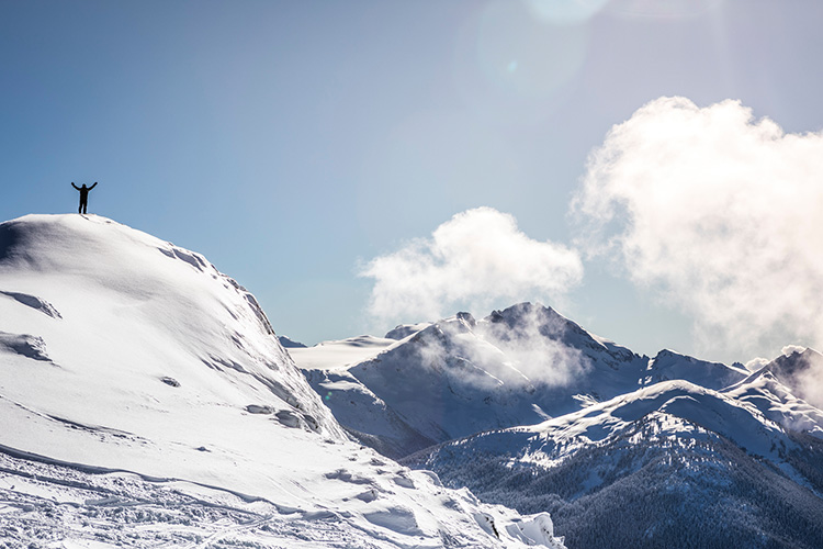 Person standing on mountain with arms in the air in Whistler