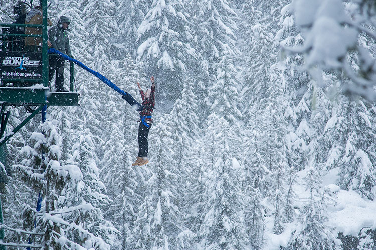 A man jumps backwards off the bridge in the snow at Whistler Bungee.