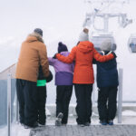 A family sightseeing in winter on Whistler Blackcomb stand looking out at the gondolas coming in.