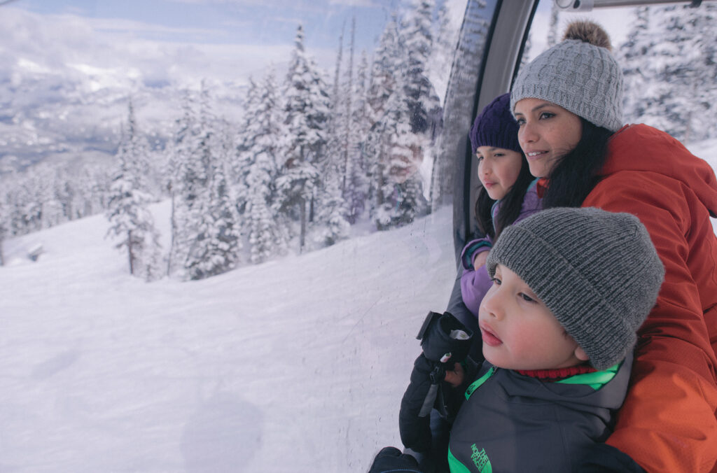 A family look out over the slopes from a covered gondola as they sightsee on Whistler Blackcomb in the winter.