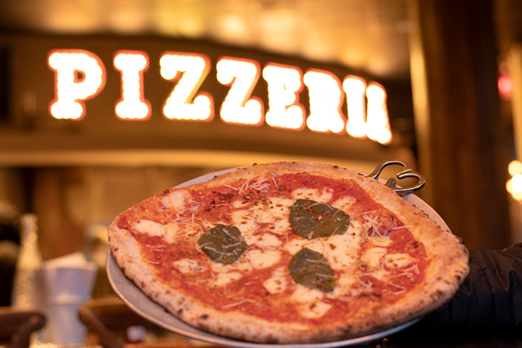 A pizza in front of a wood fire oven.