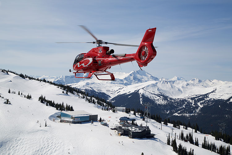 A red helicopter hovers over Blackcomb Mountain in Whistler.