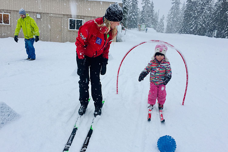 An instructor teaches a toddler how to cross country ski and Whistler Olympic Park.